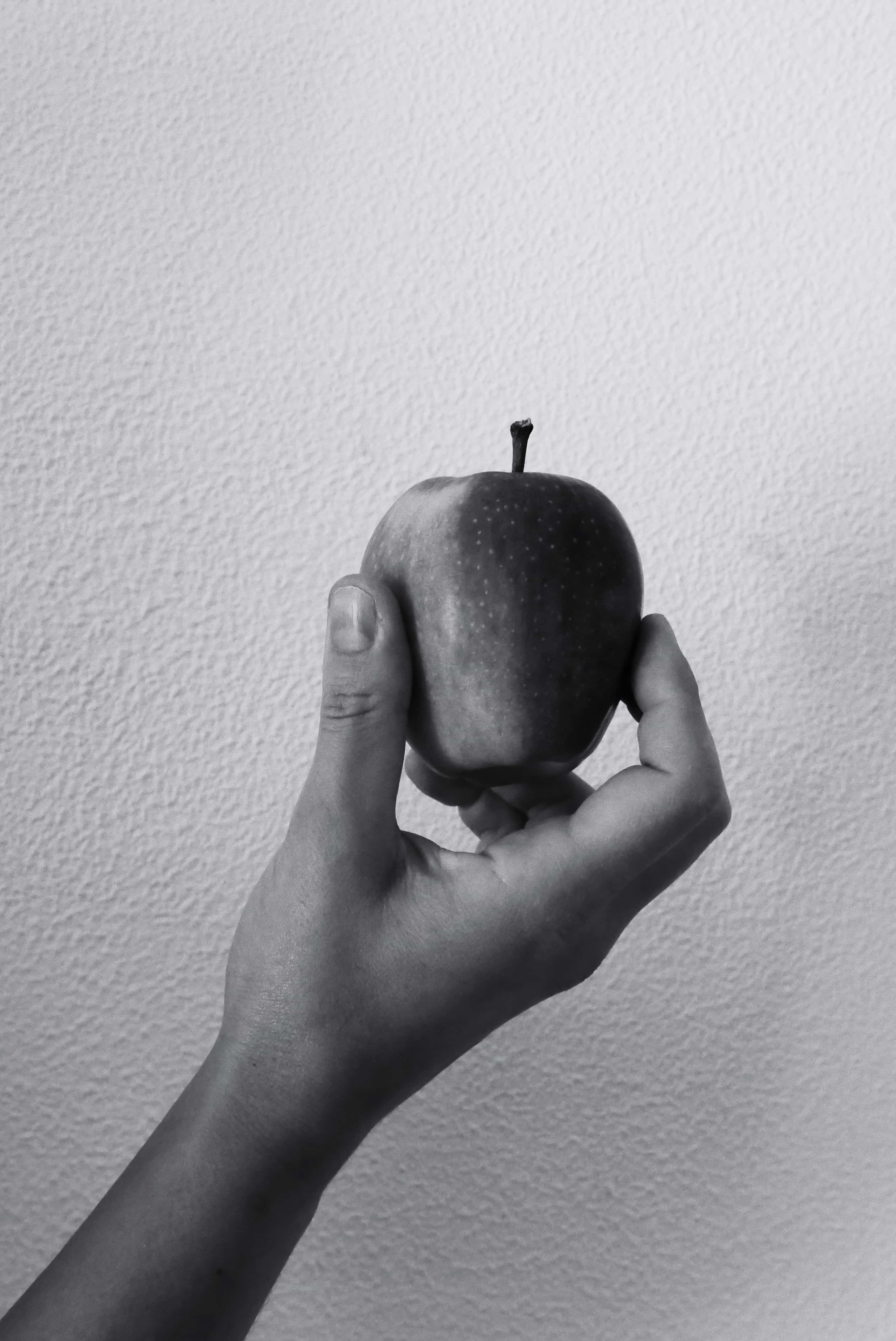 Fotorafia in bianco e nero di una mela tenuta da una mano si sfondo bianco
