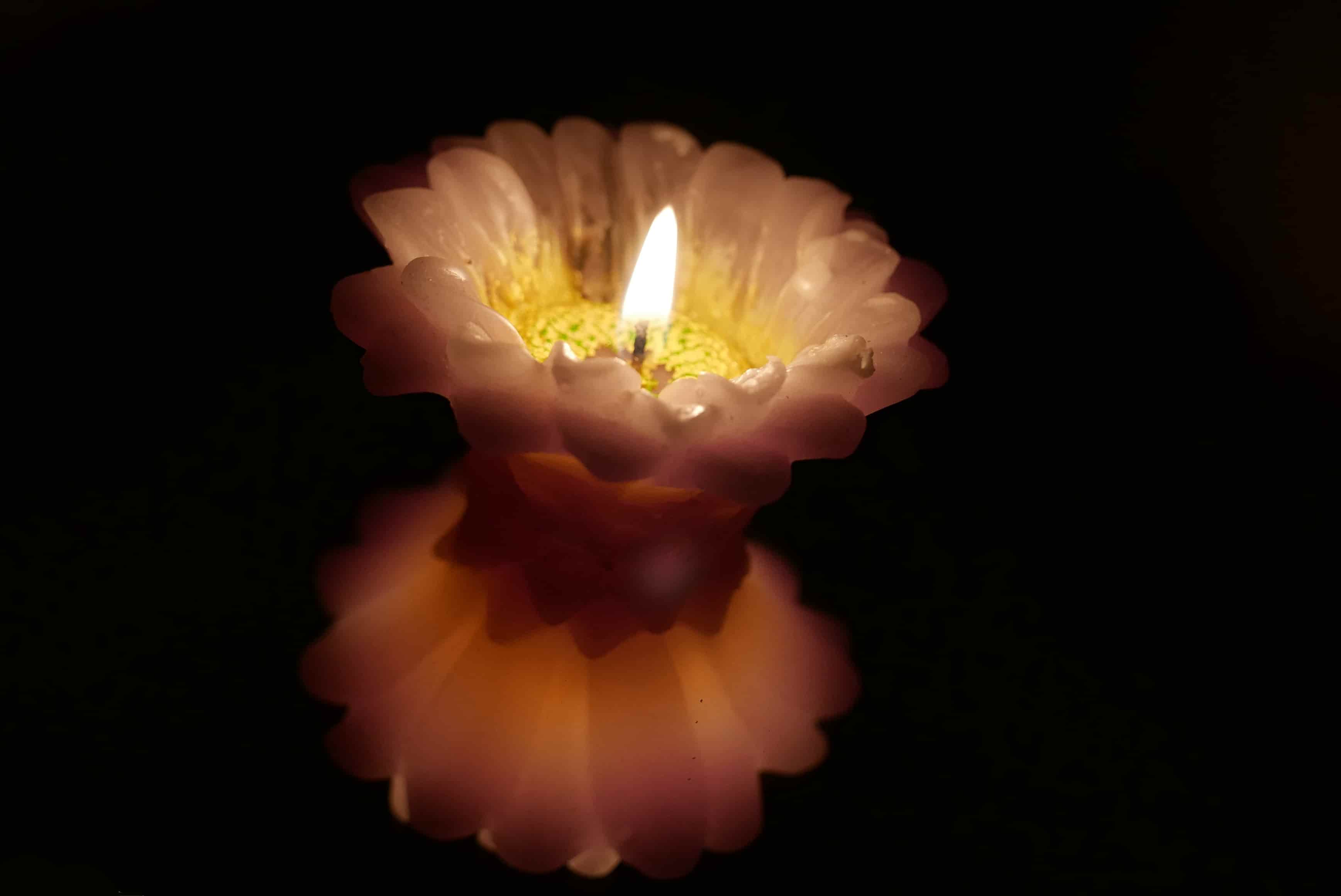 Fotografia di una candela accesa a frma di fiore riflessa nello specchio.