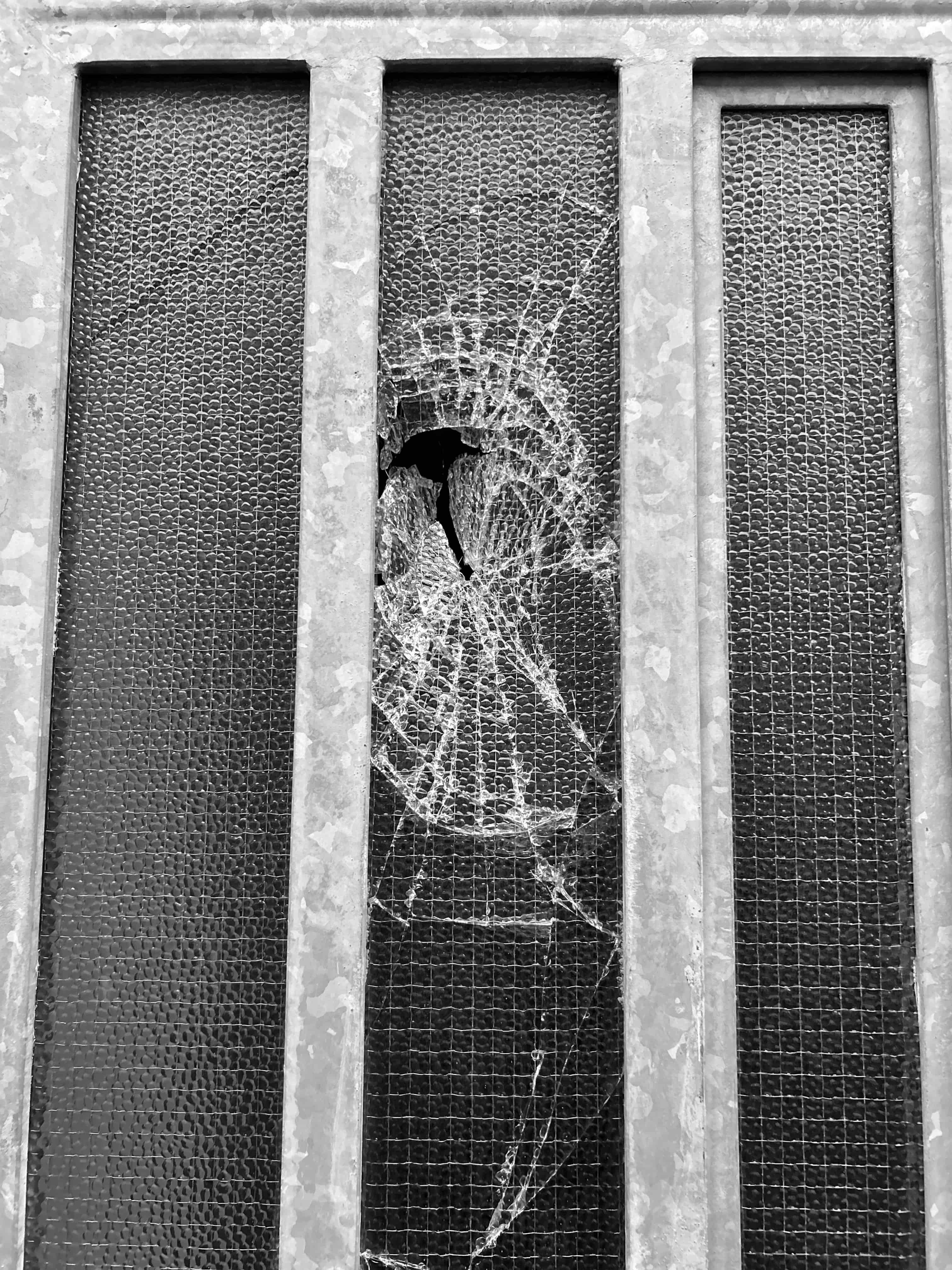 Fotografia di un vetro rotto dietro delle sbarre di ferro
