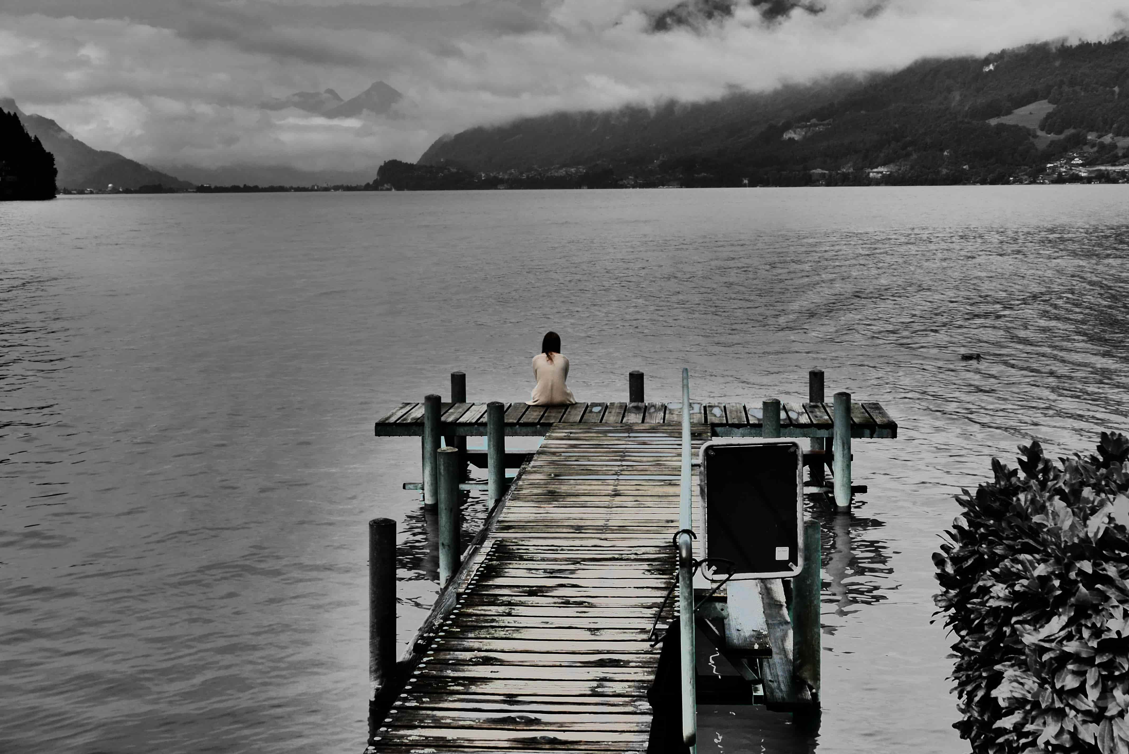Fotografia di una ragazza seduta su un molo con sfondo il lago