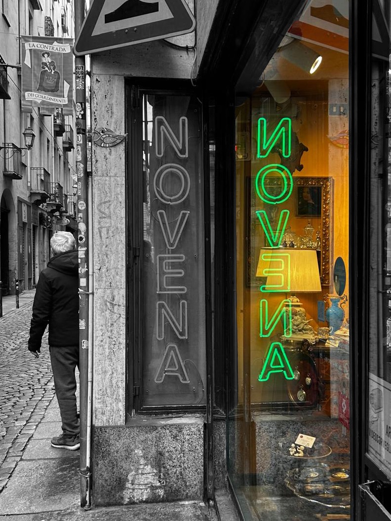 riflesso di una scritta al neon su una vetrina. a lato una persona di spalle. Il riflesso è a colori mentre il resto in bianco e nero