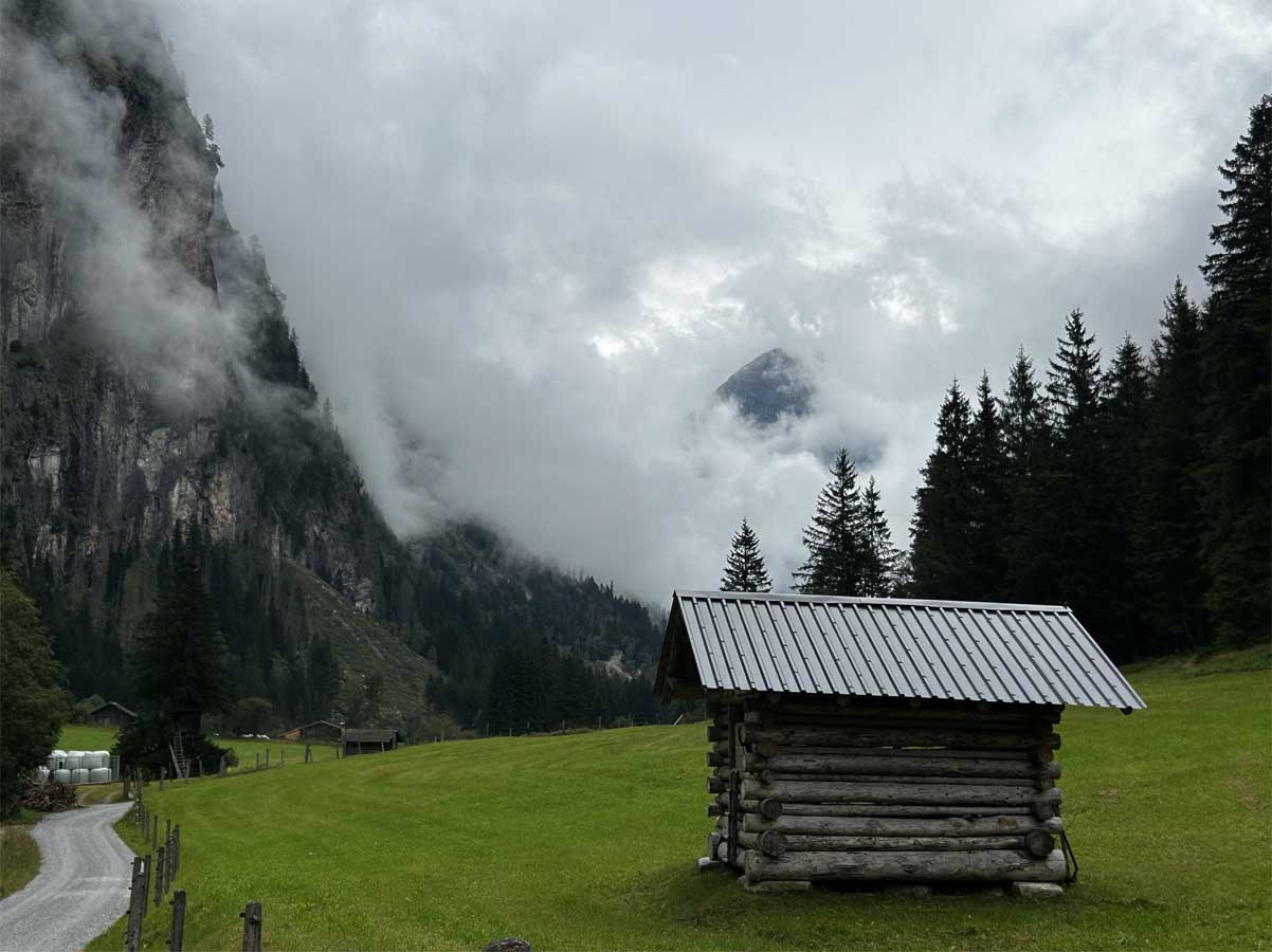 Fotografia di una piccola casa di legno in una valle tra le montagne.