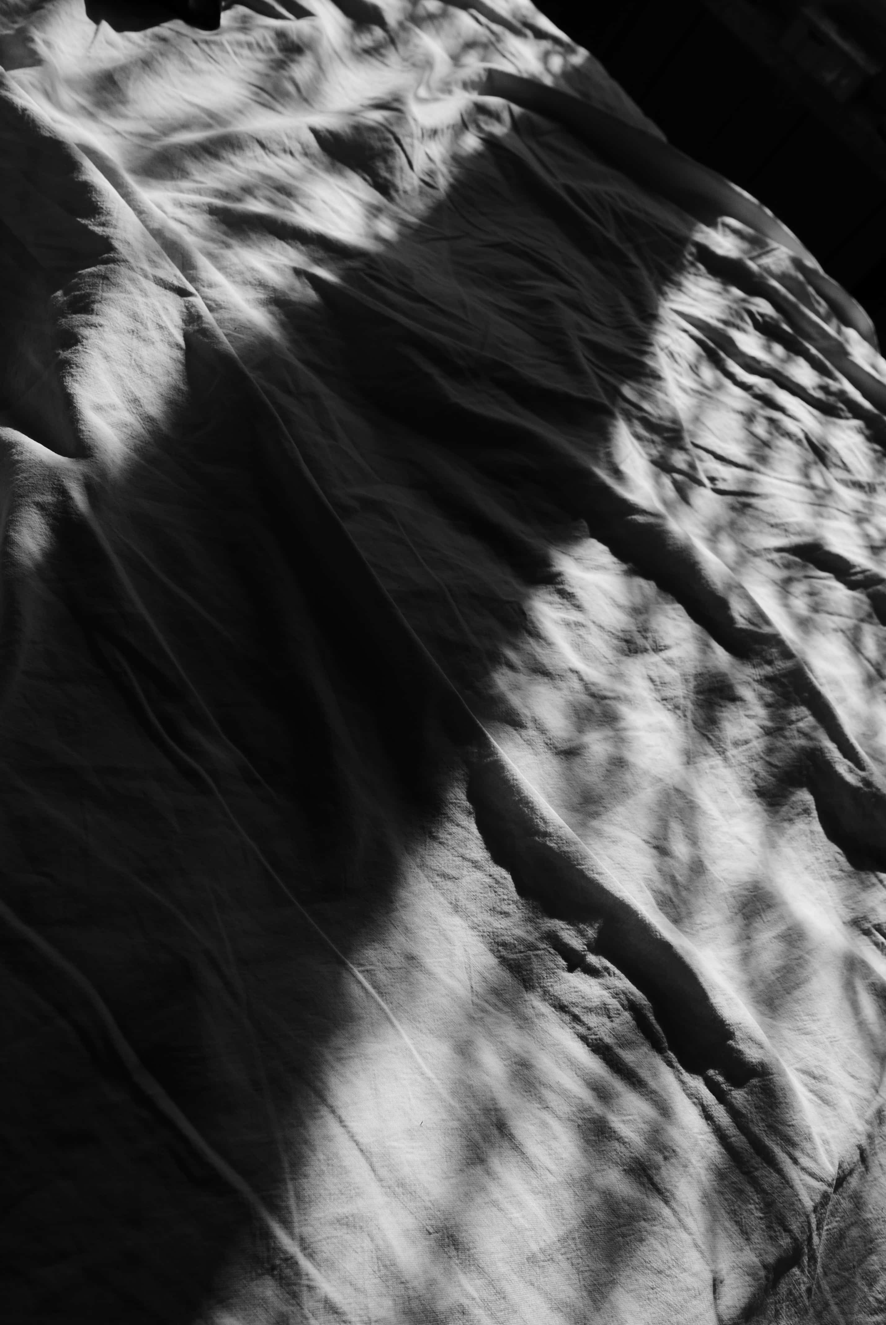 Primo piano in bianco e nero di un lenzuolo, con striature diagonali di luce e ombra che attraversano il tessuto.