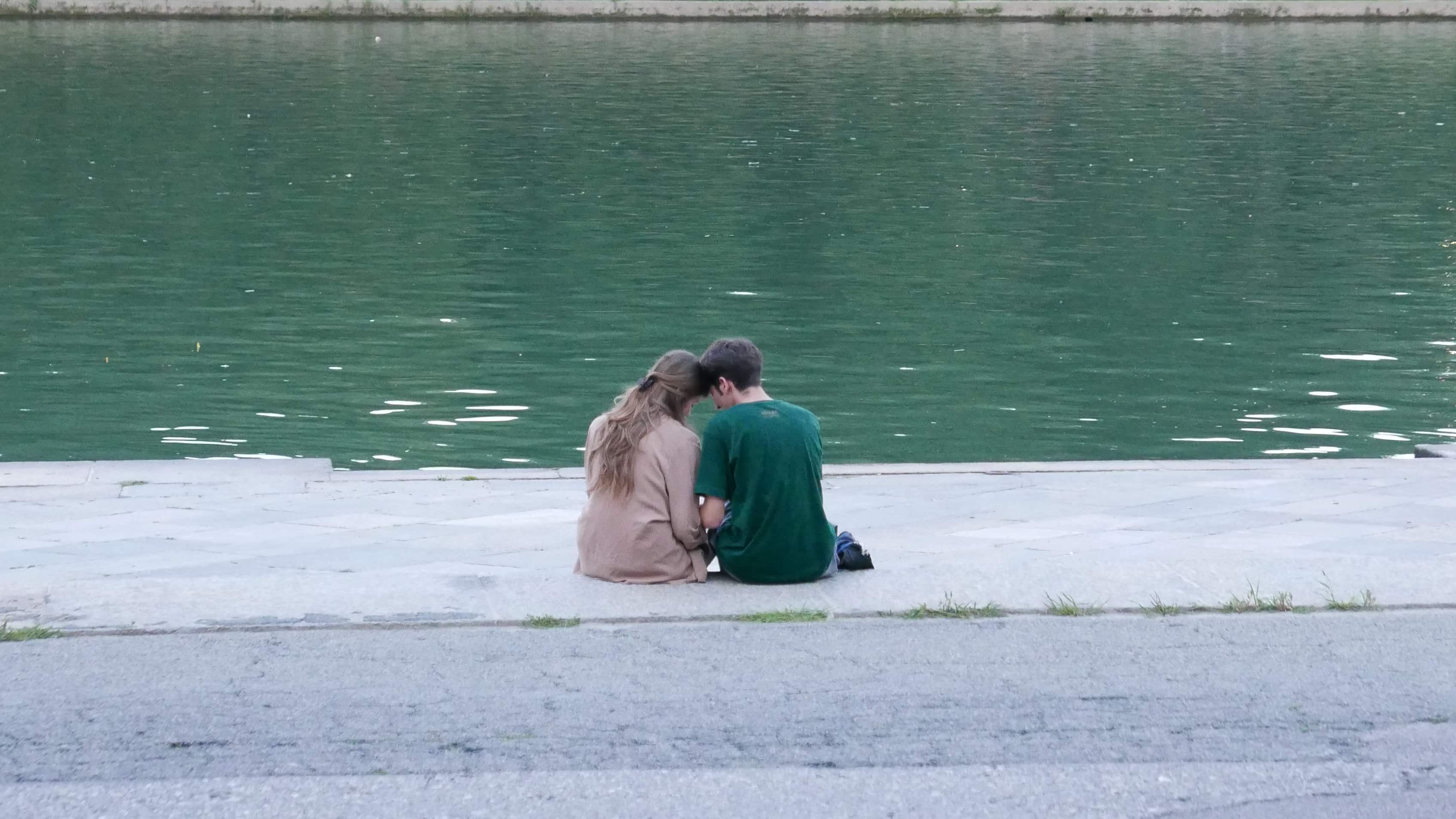 Un ragazzo e una ragazza di spalle in riva al fiume che stanno vicini in modo romantico