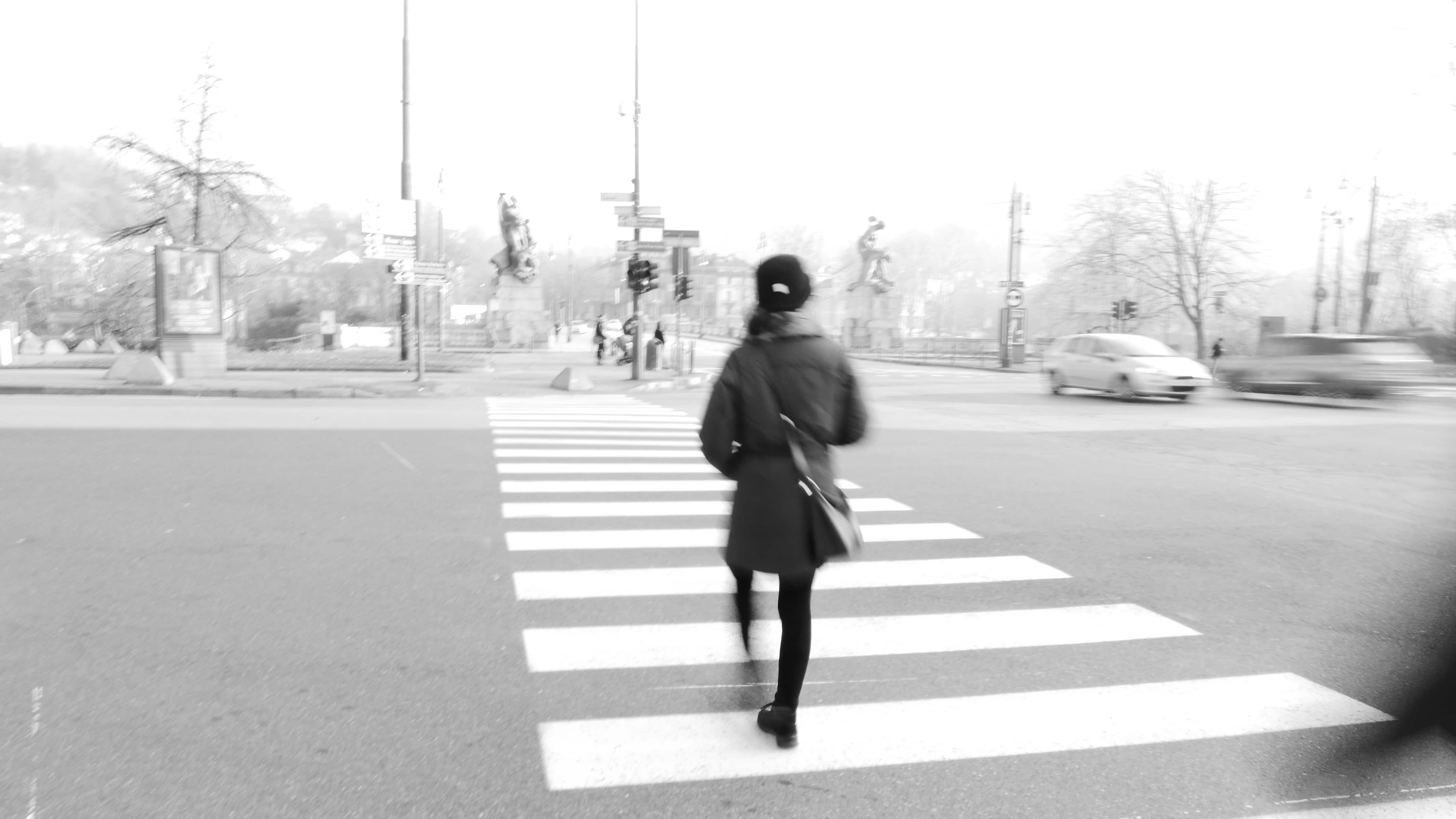 Foto in bianco e nero di una persona di spalle che attraversa la strada, tutto è sfuocato tranne lei.